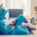 little girl in unicorn costume relaxing with mobile on couch at home