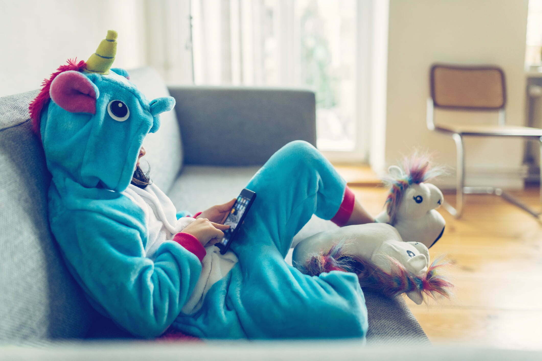 little girl in unicorn costume relaxing with mobile on couch at home